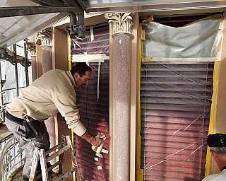 Deux ouvriers restaurent des volets rouges protégés par un film transparent sur un échafaudage