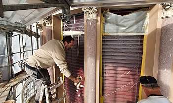 Deux hommes travaillant sur des volets rouges protégés par un film transparent lors d'une restauration