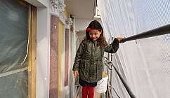 Petite fille avec veste verte et chaussettes rouges sur un échafaudage avec filet blanc