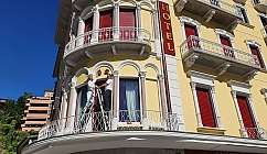 Deux hommes sur des échelles travaillent à la façade d'un hôtel avec des volets rouges