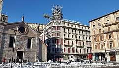 Hôtel avec échafaudages et personnes devant, à côté d'une église en pierre et de magasins en ville