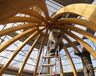 Deux ouvriers travaillent sur une structure en bois en forme de dôme avec des échafaudages autour