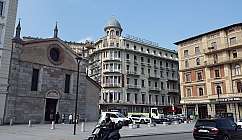 Place avec une église en pierre, hôtel avec balcons et véhicules dans la rue sous un ciel clair