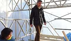 Homme en veste noire et femme assise sur un échafaudage métallique dans un environnement couvert