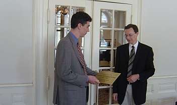 Deux hommes en tenue formelle lors de la remise d'un certificat dans une pièce élégante