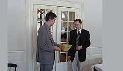 Deux hommes en tenue formelle échangent un certificat dans une pièce élégante