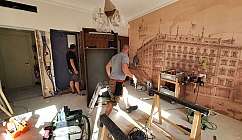 Deux ouvriers au travail dans une pièce en rénovation avec une fresque murale d'un bâtiment historique