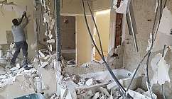 Homme démolissant des murs dans une pièce avec une baignoire et des débris sur le sol