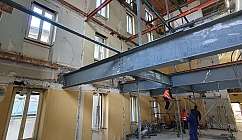 Intérieur d'un bâtiment en rénovation avec des poutres en acier et des ouvriers sur un échafaudage