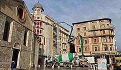 Camion toupie et grue verts devant des bâtiments historiques sur une place ensoleillée