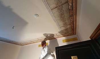 Homme avec veste blanche sous un plafond décoré avec une corniche peinte