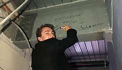 Garçon avec une veste noire écrit avec un marqueur sur une poutre métallique grise