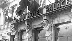 Façade historique du Grand Hotel Palace avec drapeaux, sculptures et voitures anciennes