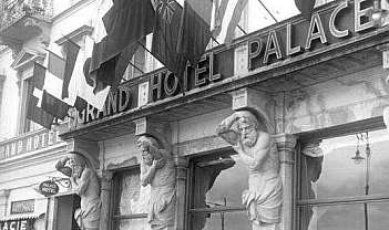 Historic exterior of the Grand Hotel Palace with flags, sculptures and vintage cars