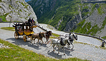 Calèche jaune tirée par quatre chevaux sur une route de montagne avec des passagers