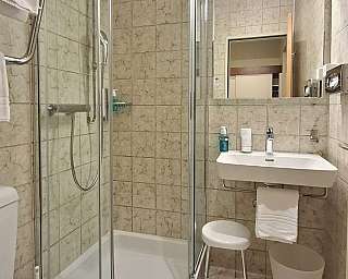 Bagno piccolo con doccia in vetro, lavabo con specchio, sgabello e bidone