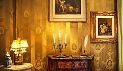 Comò antico con candelabro a tre candele, lampada e quadri dorati su parete