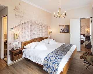 Camera d’albergo con letto matrimoniale, parete decorata, lampadario e specchio