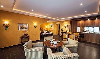 Grand séjour avec fauteuils, table, lit, cuisine et éclairage chaleureux