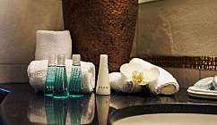 Set cortesia con bottigliette, asciugamani bianchi e fiore su piano bagno lucido