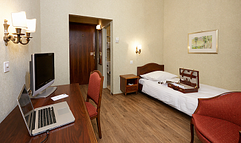 Camera d’albergo con letto singolo, scrivania con laptop e TV, sedia e poltrona rossa