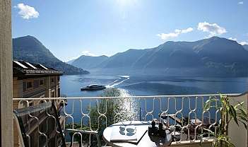 Balcone con tavolo, sedia e pianta con vista su lago e montagne al tramonto