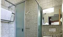 Bagno piccolo con doccia angolare, WC con sedile nero e lavabo con specchio