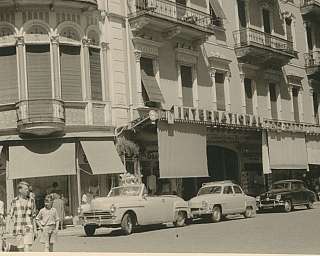 Blick auf ein historisches Gebäude mit Oldtimern und Passanten.