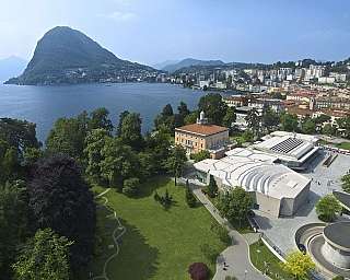 Panorama of Lake Lugano with surrounding mountains and buildings.