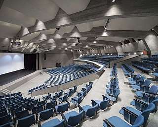 Interior of an auditorium with blue chairs and a stage.