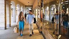 Couple marchant main dans la main sous un portique avec des vitrines de magasins