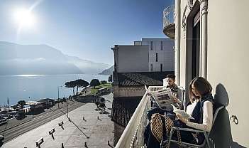 Due persone sul balcone leggono, vista sul lago e montagne.