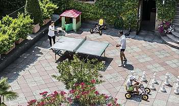 Due persone giocano a ping pong in un cortile fiorito.