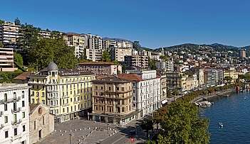 Vue du bord du lac de Lugano avec des bâtiments et des arbres.