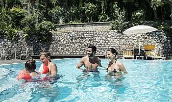 Deux adultes et deux enfants jouant dans une piscine extérieure avec parasol et chaises longues