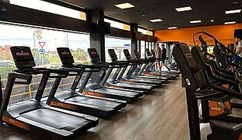 Innenraum eines Fitnessstudios mit einer Reihe von Laufbändern und trainierenden Personen