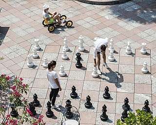 Zwei Personen spielen Schach in einem Park, mit einem Kind auf einem Fahrrad.