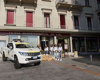 A group of people in front of a hotel with a parked car.