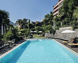 Vue d'une piscine entourée de plantes et de chaises longues dans le jardin.