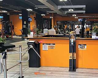 Reception di palestra con tornello, distributore di bevande e attrezzi fitness sullo sfondo