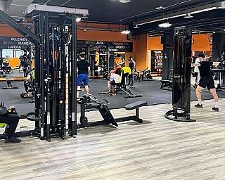 Interno di una palestra con persone che si allenano usando attrezzi moderni e pavimento in legno