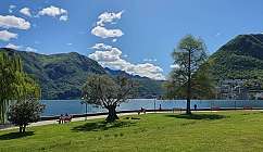 Parc vert du Belvédère, bancs et personnes près d'un lac avec des montagnes en arrière-plan