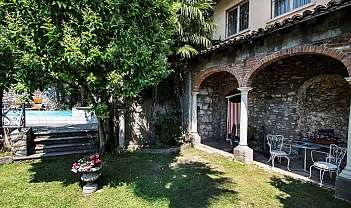 Jardin avec pelouse, arbre, piscine, porche avec arches en briques et chaises blanches