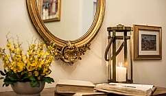 Miroir ovale doré, vase avec des fleurs jaunes, livres ouverts et lanterne avec bougie allumée sur la table