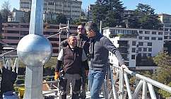 Trois hommes souriants sur une plateforme de travail en hauteur.