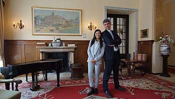 Due persone in abiti formali in un salotto con pianoforte e camino