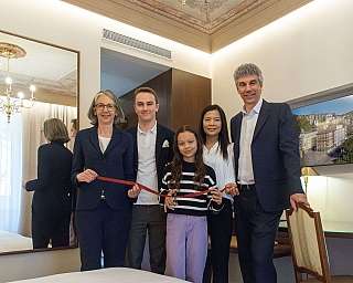 Cinque persone sorridenti in una stanza d'hotel durante una cerimonia di taglio del nastro