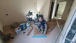 A man is laying a wooden floor in a room under renovation.