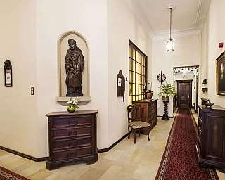 Corridoio con statue, mobili in legno e piante decorative.