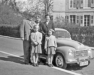Una famiglia in posa accanto a un'auto vintage.